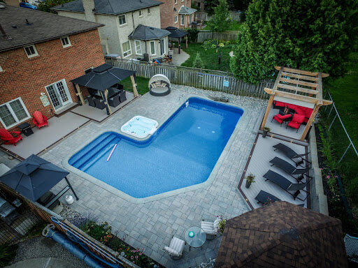 A backyard with an L-shaped pool and a stone patio.