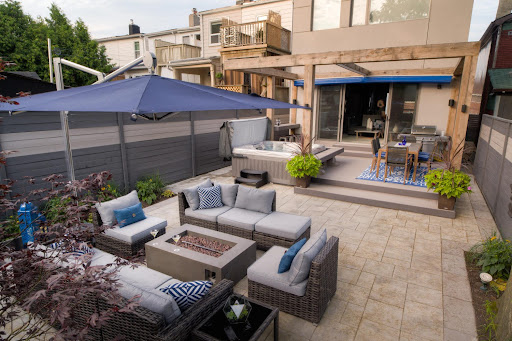 A stone patio in a backyard with a seating area, fire table, and hot tub.