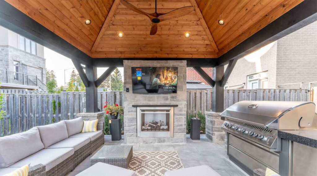 Outdoor pavilion with fireplace and TV, creating a cozy living-room-style seating area in the backyard