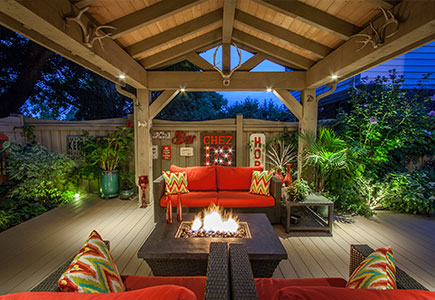 Cottage-style backyard in Etobicoke featuring a PVC deck, timber roof with exposed rafters, cozy fire table seating, dining area, and lush surrounding gardens.