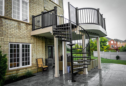 Second-floor Brampton deck with diagonal composite decking, curved corners, custom railings, and a compact spiral staircase to the lower level.