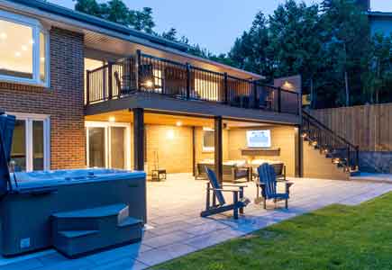 Modern second-floor walkout deck with waterproofed lounge area below, fireplace feature wall, and ravine views — Mississauga backyard renovation.