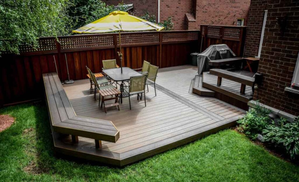 Two-level low-profile Trex composite deck with a dining area on the lower level and a BBQ space on the upper deck, opening into a grassed backyard