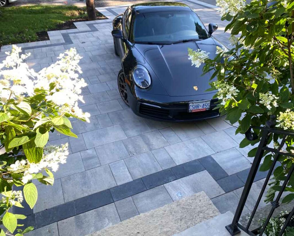 Interlocking stone driveway in Etobicoke with a finished hardscape design, luxury vehicle, and flowering garden beds