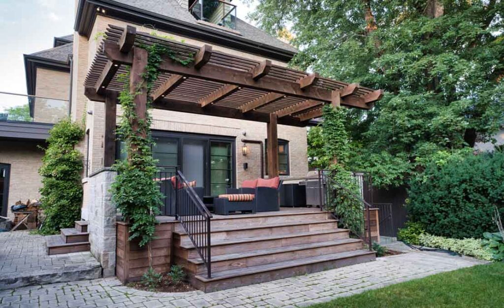 Heat-treated wood deck off the main floor in Mississauga with a timber pergola, integrated lighting, and wisteria providing natural shade for seating and a cooking area