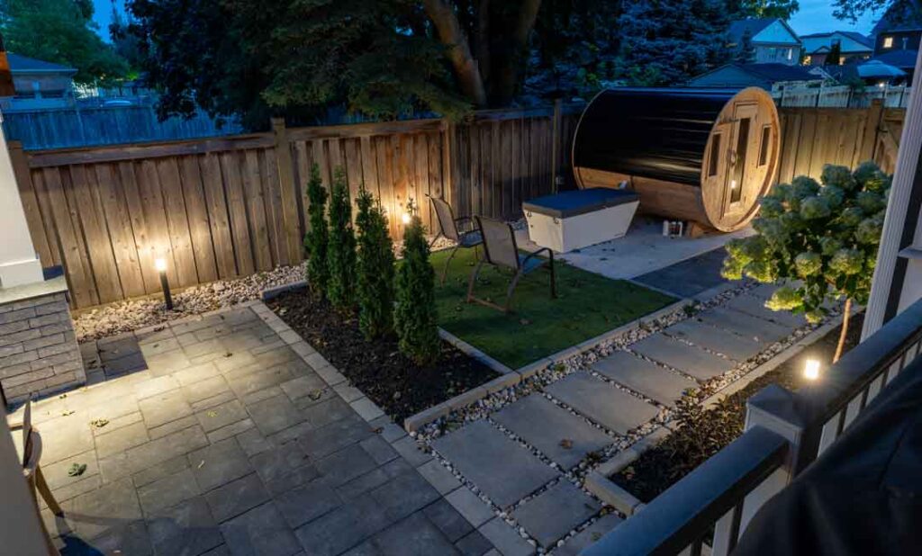 Evening backyard landscaping illuminated with outdoor lighting highlighting gardens, pathways, and a fitness area for nighttime use.