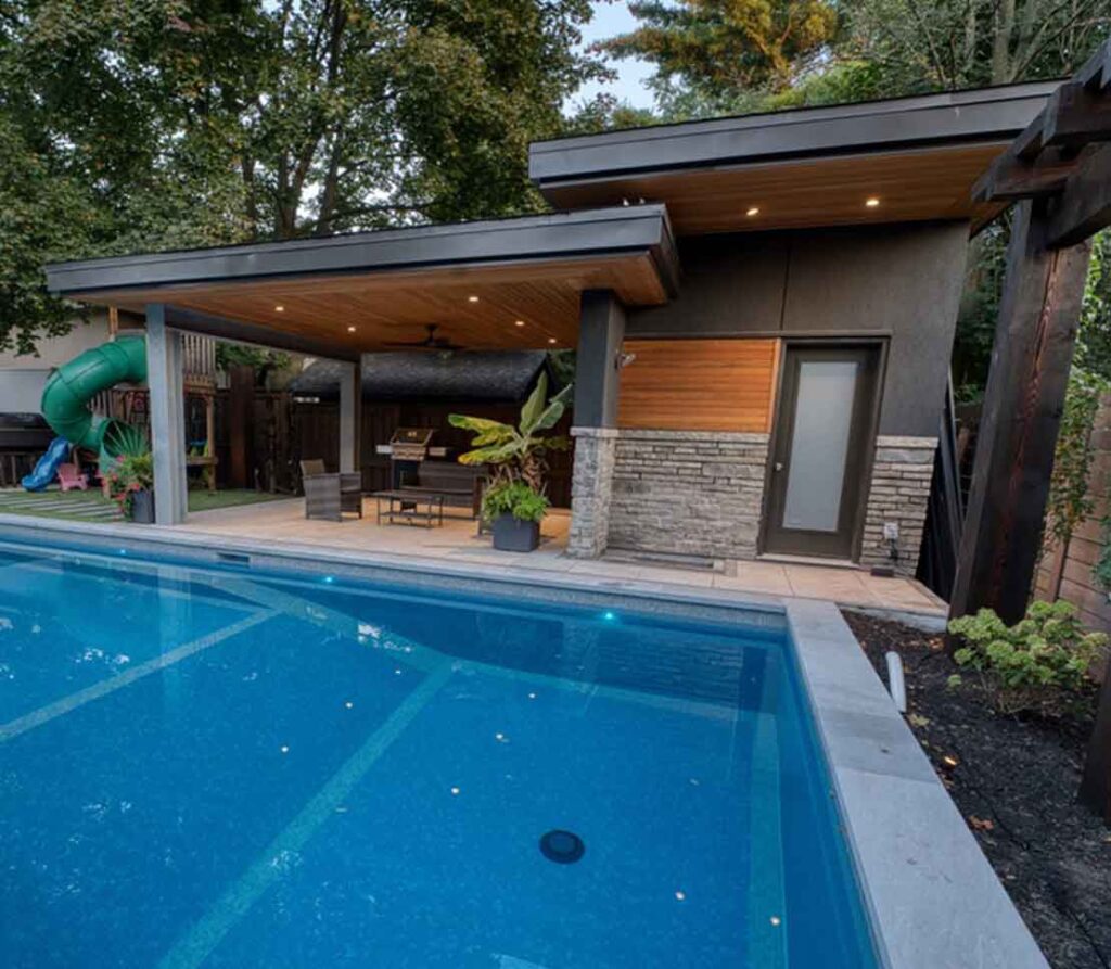 Modern cabana with stone and stucco finishes, a warm wood ceiling, and an integrated shed and washroom, designed to seamlessly complement the pool area.