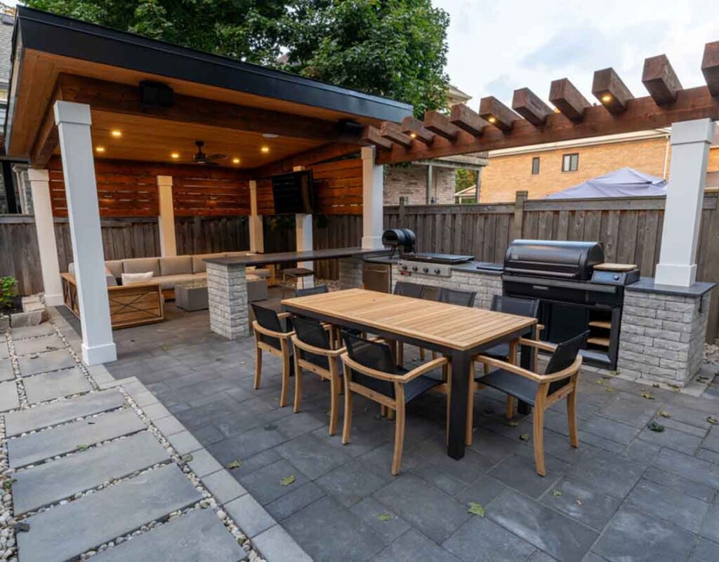 Modern cabana in Mississauga with a cozy lounging area under the roof, TV feature wall, bar seating, and a fully equipped outdoor kitchen, all warmly lit for evening entertaining.