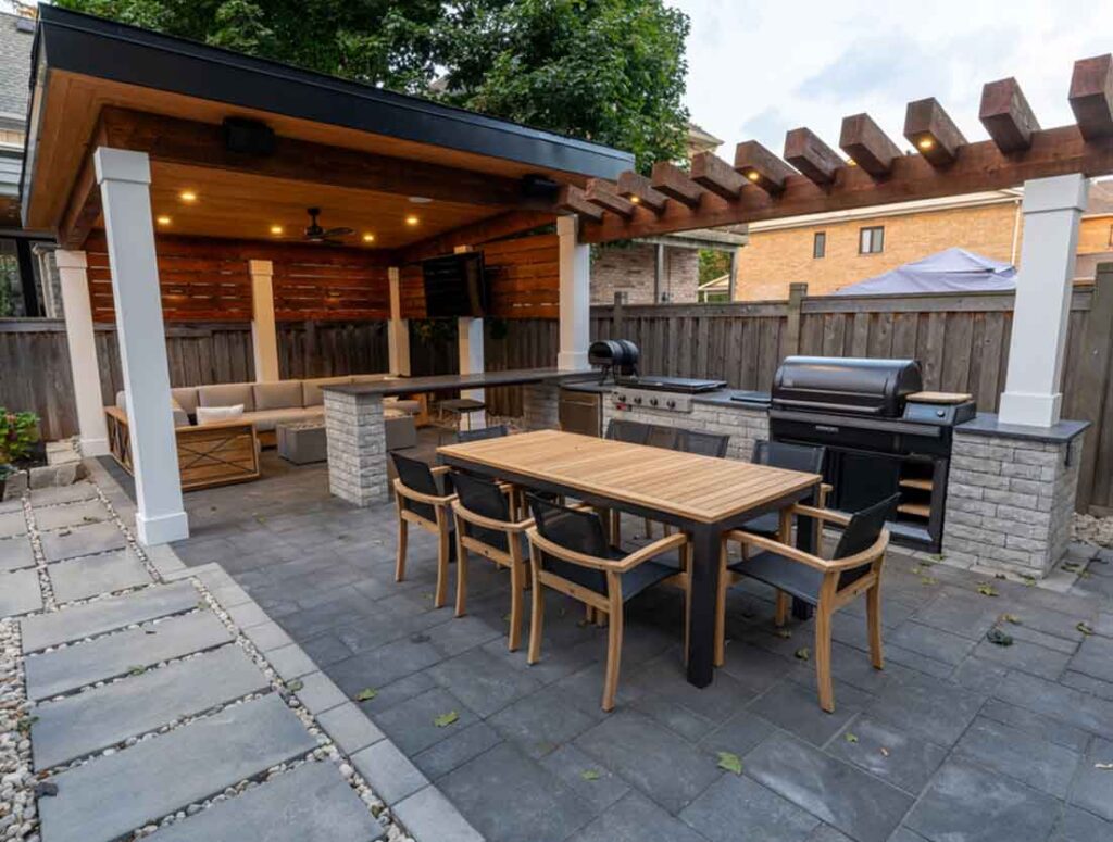 Modern pavilion in Mississauga with integrated lighting, TV feature wall, comfortable lounging area, attached bar top, and an outdoor kitchen with a large dining table for entertaining.