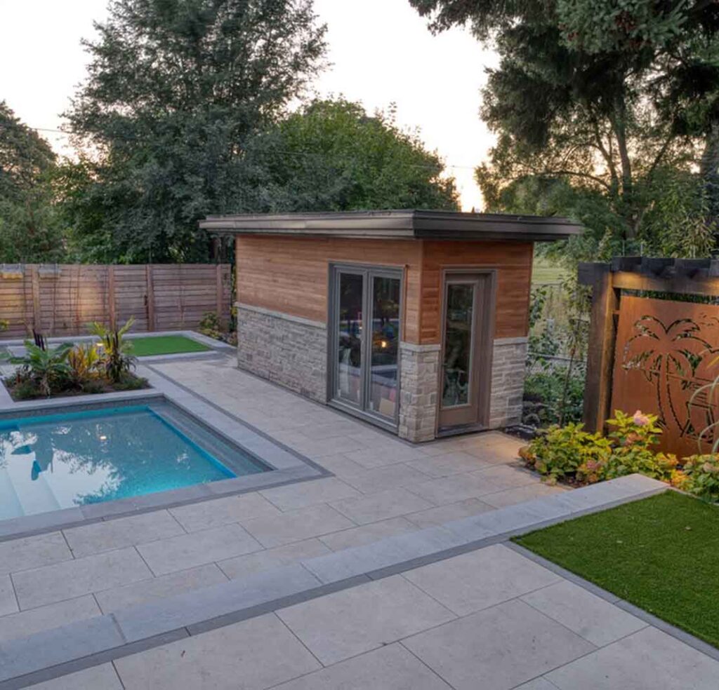 Modern pool surrounded by a stone patio with integrated planter, custom shed, and landscaped greenery