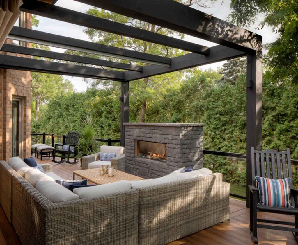 Modern timber pergola with a ShadeFX retractable awning over a lounge area with a fireplace, creating a cozy setting for evening relaxation