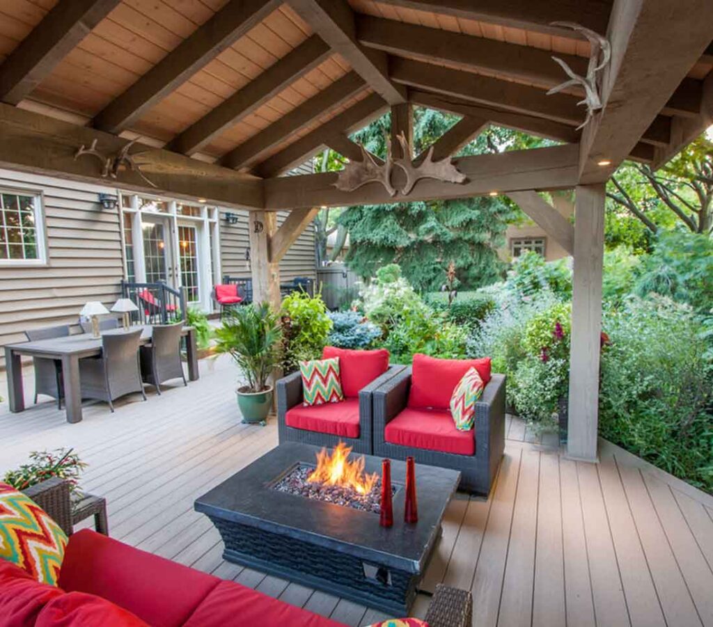 Timber pavilion styled as a staycation retreat, featuring a fire pit and comfortable seating on a deck, surrounded by lush greenery for a resort-like outdoor feel.