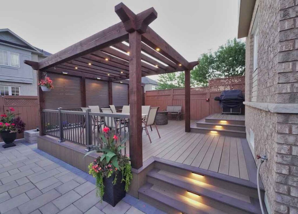 PVC deck in Ancaster with a timber pergola, integrated lighting, and a cozy seating area with a fireplace, designed across two levels to create visual interest and functional outdoor living