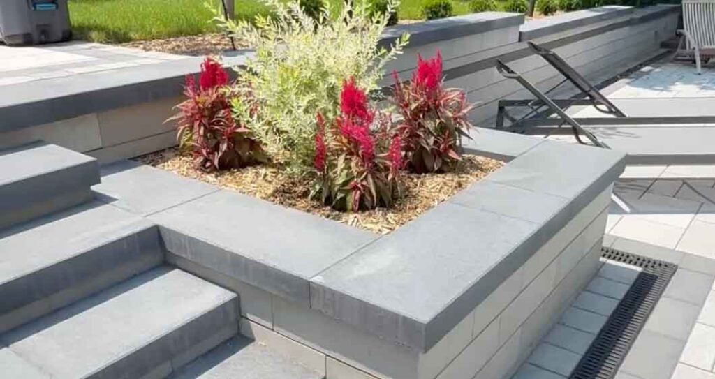 “Concrete block retaining wall around a pool, seamlessly integrated with a planter and stairs, built using Oaks Pavers.