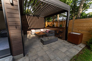 Toronto backyard with louvered pergola, three-season room addition, and fire table seating area.