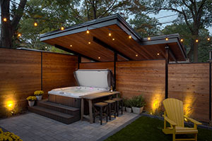 Beaches Toronto backyard landscaping with hot tub, artificial turf, landscape lighting, planting beds, and custom roof cover doubling as rear carport