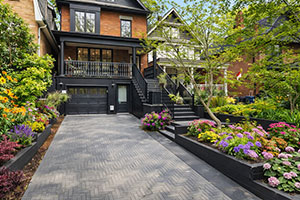 Modern front yard landscape design featuring interlock driveway, layered planting beds, and natural stone steps leading to the front porch.