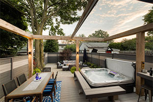 Toronto Beaches backyard landscaping with natural stone patio, timber pergola with retractable awning, hot tub, and fire table lounge area.