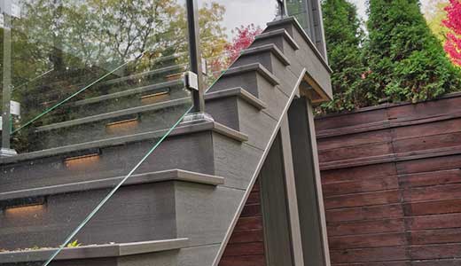 Side profile of second floor deck stairs with closed riser returns, glass railings, and integrated stair lighting