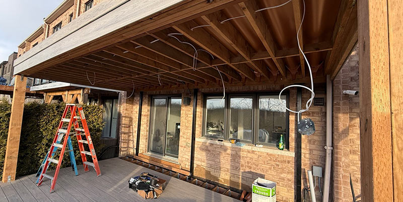 Elevated deck frame with RainEscape waterproofing system emphasizes prepped wiring for lights and ceiling fan before wood ceiling installation