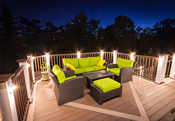 Evening photo of a second-floor deck featuring illuminated railings and a seating area overlooking a ravine