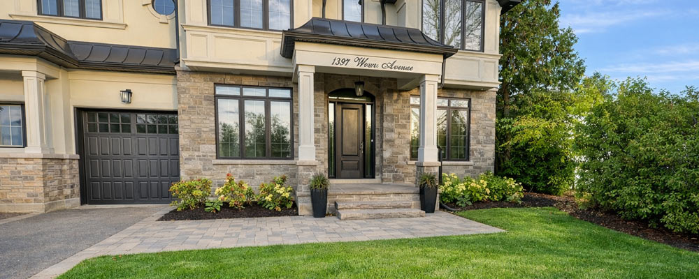 Oakville front yard landscaping with widened driveway, covered natural stone front porch, and expansive side garden beds for a refined curb appeal.