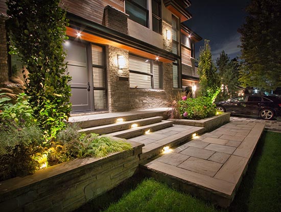 Modern front yard landscaping with natural stone walkway, large gardens, and evening lighting