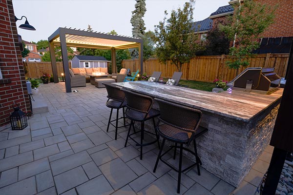 Simple modern backyard in Toronto featuring an outdoor kitchen with bar, hot tub, and louvered pergola with fire table designed for effortless outdoor living.