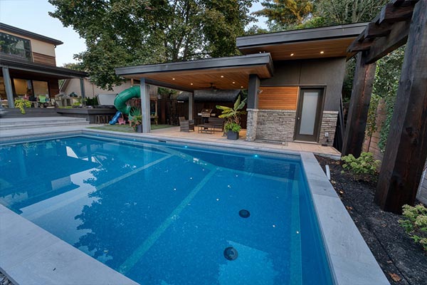 Modern Toronto backyard with tile pool and contemporary cabana lounge, seamlessly integrated with the home to create a private backyard oasis.