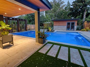 Luxury backyard with modern tiled pool, pool house, and covered lounge under roof overhang
