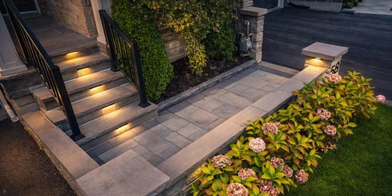 Natural stone front porch with integrated step lighting, aluminum railings, and landscaped knee wall in evening setting