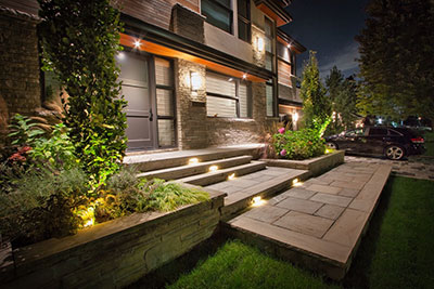 Concrete raised planters faced with natural stone veneer integrated with natural stone steps, planting, and landscape lighting in a Mississauga backyard