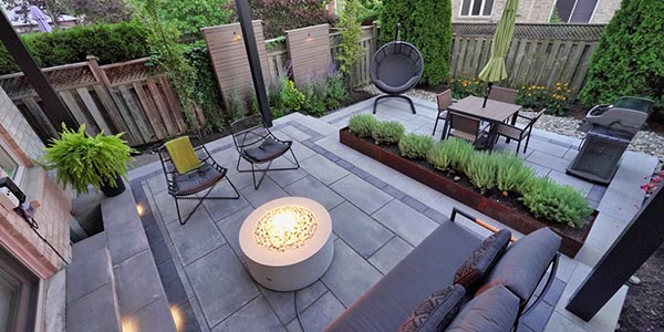 Luxury townhome backyard with multilevel stone patio, louvered pergola, corten steel planter, fire pit, and layered planting
