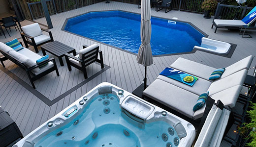 On-ground pool surrounded by a deck with integrated hot tub and louvered pergola