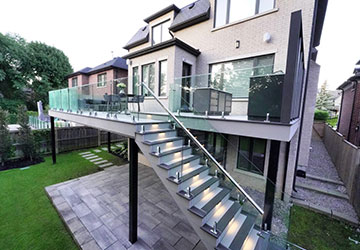 Custom steel-framed second-floor deck with frameless glass railing, outdoor kitchen, and architectural lighting