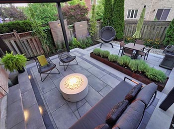 Townhome backyard stone patio with two levels, lush planting, and louvered pergola