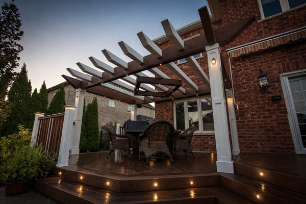 Custom pergola structure over backyard deck with outdoor dining area and built-in lighting