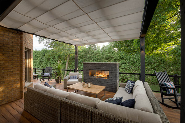 Composite deck with pergola and ShadeFX retractable awning, seating area and fireplace with glass railings overlooking greenery