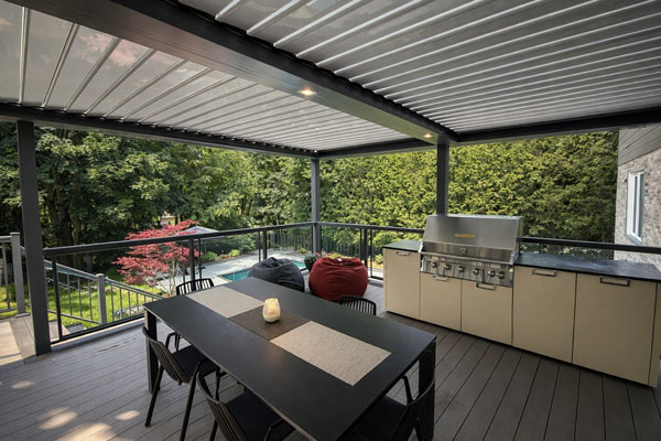 Louvered pergola over a composite deck with outdoor kitchen and dining area overlooking a backyard pool