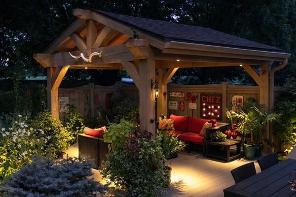 Wood backyard gazebo with outdoor lounge seating and evening lighting surrounded by garden landscaping